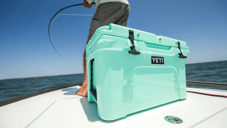 The 5 Best Boat Coolers, According to Experts Person fishing on boat with seafoam green YETI cooler in foreground.
