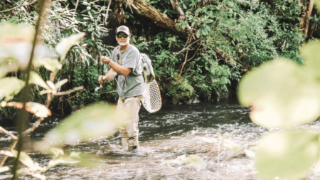 The 5 Best Hip Waders Man fly fishing in a forest stream wearing waders and carrying a net.