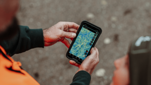 Two workers in safety gear reviewing a digital map on a rugged smartphone outdoors.