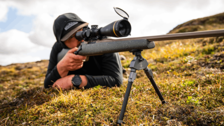 Hunter prone on tundra aiming bolt-action rifle with scope and bipod