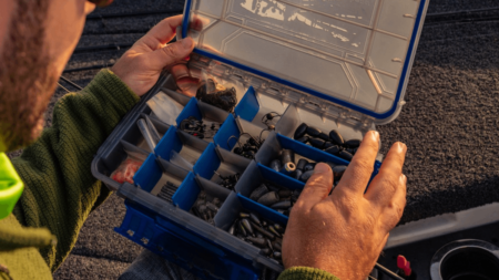 Person opening blue tackle box filled with fishing weights and terminal tackle components.