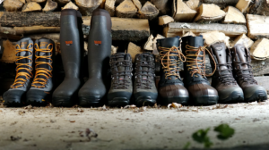 Five pairs of hunting and hiking boots displayed against a rustic firewood stack.