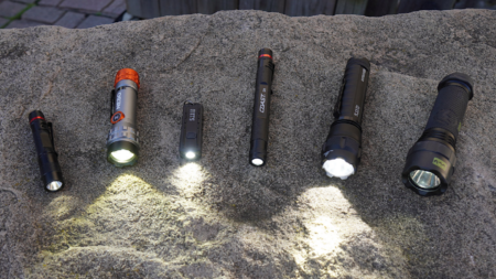 Six LED flashlights of varying sizes displayed on stone surface with beams illuminated.