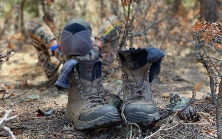 The Best Elk Hunting Boots of 2024, Expert Tested Hunter resting in forest with muddy hiking boots and socks in foreground
