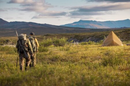 The Future of 28 Million Acres of Public Land in Alaska Hangs in the Balance Two camouflaged hunters with backpacks approach a tent in remote mountain wilderness.