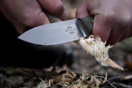 Person using White River USA fixed blade knife to carve wood shavings outdoors.