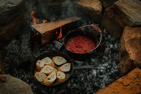 The 6 Best Dutch Ovens for Camping (2024 Review) Cast iron campfire cooking with tomato sauce and toasted bread slices outdoors.