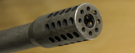 Close-up view of a perforated metal gun muzzle brake on a rifle barrel