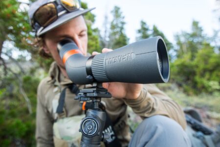 Best Spotting Scopes for Birding of 2024 Person looking through Maven spotting scope mounted on tripod outdoors in nature.