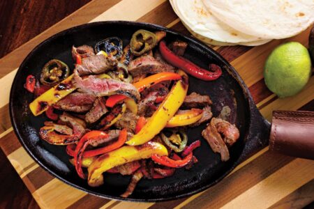 Sizzling steak fajitas with colorful bell peppers in cast iron skillet with tortillas
