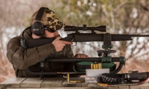 Man aiming bolt-action rifle with scope at outdoor shooting range bench rest