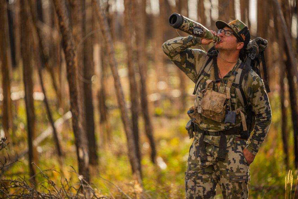Hunter in camouflage gear drinking from container in autumn forest woodland.
