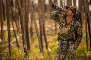 Hunter in camouflage gear drinking from container in autumn forest woodland.