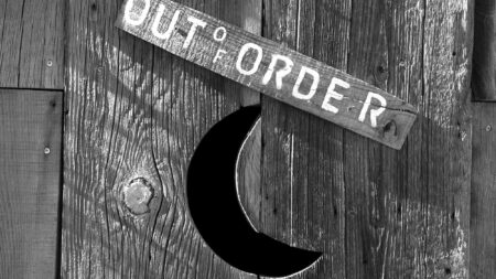Rustic wooden outhouse door with crescent moon cutout and Out of Order sign