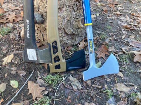 Two axes leaning against a tree: Fiskars hatchet and Estwing camp axe outdoors.