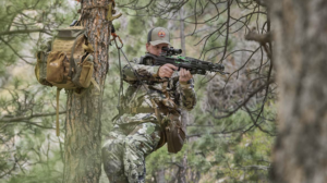 Hunter in camouflage aiming crossbow from tree stand in forest