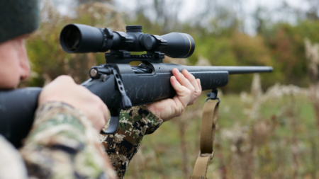 The 35 Best Gun Deals This Week Person in camouflage aiming bolt-action rifle with scope outdoors in field