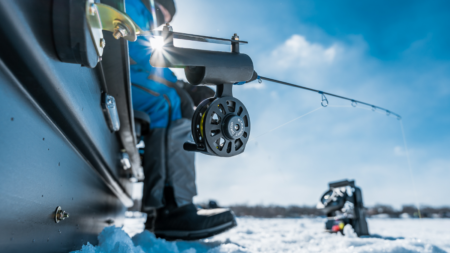 Person ice fishing outdoors in winter with fishing rod and reel on snow.