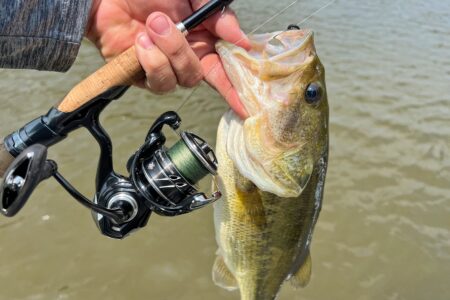 Daiwa Tatula MQ LT, Tested and Reviewed Angler holding largemouth bass caught with spinning rod and reel over water