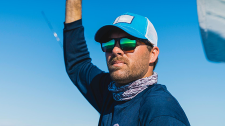 Man wearing blue cap and green mirrored sunglasses outdoors on sunny day