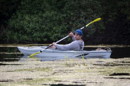 Young man kayaking on a calm, algae-covered lake with yellow paddle
