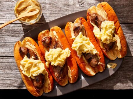 The Complete Guide to Making Wild Game Sausage Four bratwurst sausage sandwiches topped with scrambled eggs and mustard on a platter.