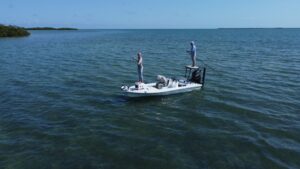 Two anglers standing on a small fishing boat in calm turquoise waters.