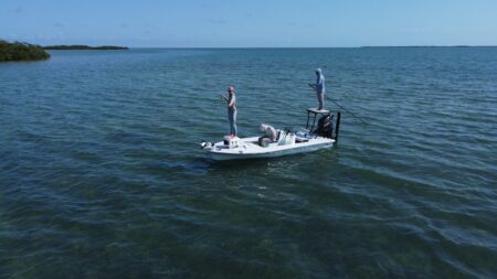 Two anglers standing on a small fishing boat in calm turquoise waters.
