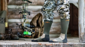 Hunter wearing camouflage pants and green Darn Tough hunting socks on wooden porch