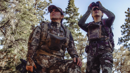 The 6 Best Women-Owned Hunting and Fishing Brands of 2024 Two female hunters in camouflage gear scanning forest with binoculars outdoors.