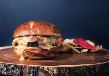 What’s the Perfect Venison Burger Recipe? Gourmet cheeseburger with caramelized onions on pretzel bun served with vegetable chips