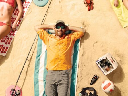 31 Ways to Have the Best Summer Ever Man in orange shirt relaxing on striped towel at sunny beach surrounded by gear