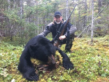 Hunter posing with harvested black bear in forest holding rifle