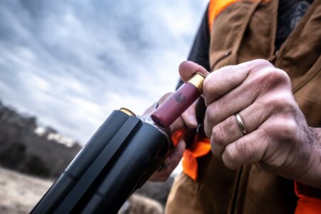 How to Load a Shotgun Hunter in orange vest loading shotgun shells into a double-barrel shotgun outdoors.