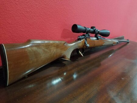 Bolt-action hunting rifle with walnut stock and telescopic scope on wooden table