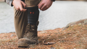 Person adjusting dark hiking socks over laced brown boots near a river.
