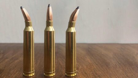 7mm Rem Mag: A Weak-Kneed and Flaccid Magnum Three brass rifle cartridges with pointed bullets standing upright on wooden surface