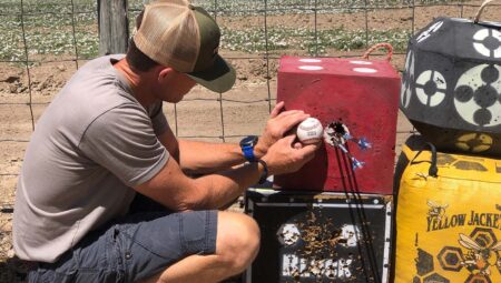 Man examines baseball lodged in archery target block outdoors near fence