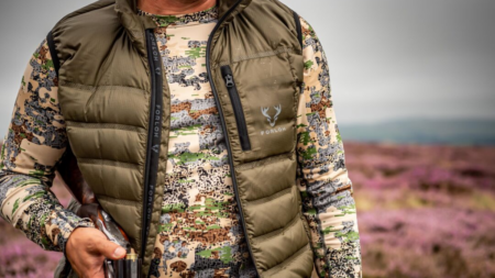 The Best (and Warmest) Hunting Base Layers Person wearing Forloh hunting vest and camouflage jacket holding a shotgun outdoors.