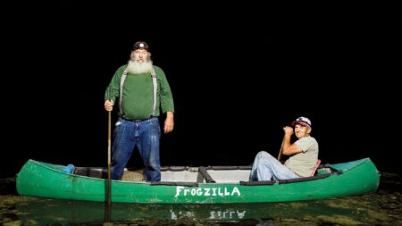 Two men in a green canoe named Frogzilla on dark water at night.