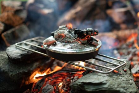 Cast iron skillet with hot coals cooking over open campfire on stone hearth