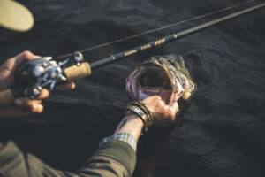 Angler holding a largemouth bass with baitcasting rod over dark water