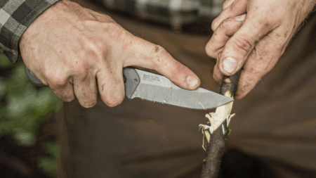 Weathered hands using a Made in USA folding knife to whittle a wooden stick