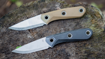 Two Gerber fixed blade knives with tan and black handles on wood stump