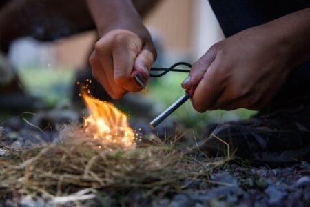 Four Survival Myths That Could Get You Killed Hands using a ferro rod fire starter to ignite dry grass tinder outdoors