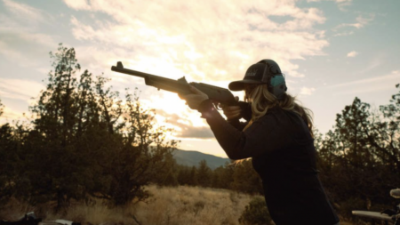 Woman aiming rifle at outdoor shooting range during golden hour sunset