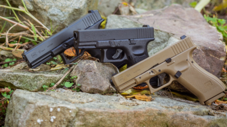 The Best Air Pistols of 2024 Three Glock pistols resting on outdoor rocks, two black and one tan.