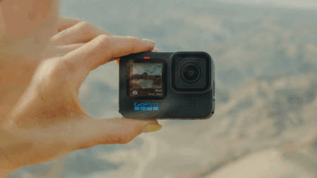 Hand holding a GoPro action camera displaying burst mode in outdoor setting.