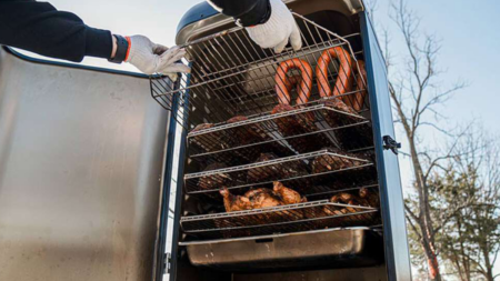 The 5 Best Electric Smokers of 2024, According to Our Hands-On Tests Person wearing gloves removing smoked meats from a multi-rack outdoor smoker grill.