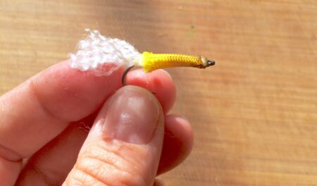 Hand holding a yellow and white fly fishing lure with hook close-up